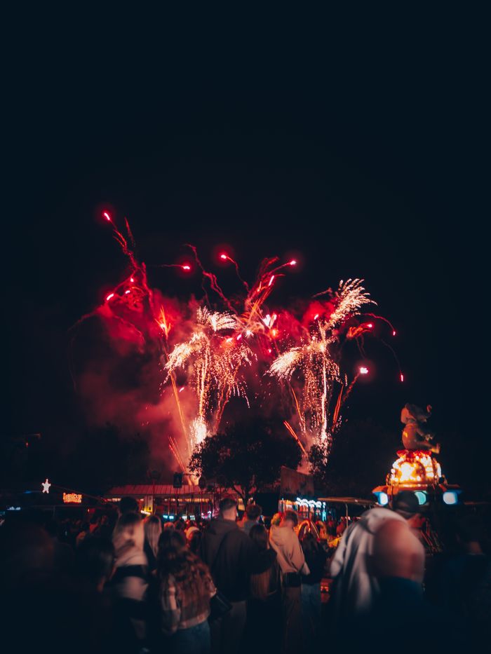 Crowd enjoying stunning night fireworks at a bustling funfair in Landau, Germany.
