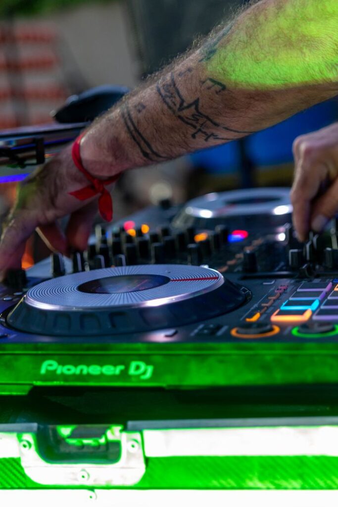 A tattooed DJ's hands skillfully navigate a Pioneer mixer during an energetic club event.