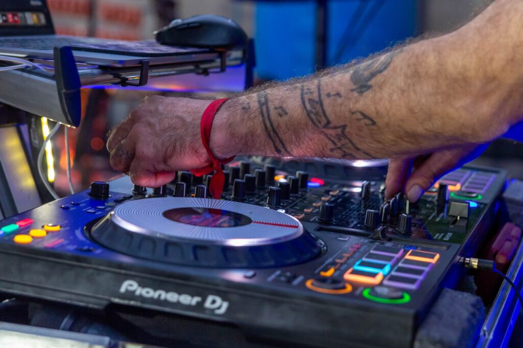 DJ's hand mixing music on Pioneer turntables with vivid stage lighting at a live event.